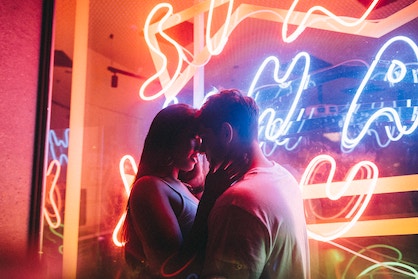 A guy and girl standing next to neon signs about kiss