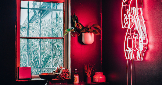 A red room with a neon light, a table, three plants and a diffuser