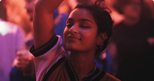 A lady with her eyes closed dancing with her hands up in a club
