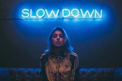 A lady wearing an Adidas jacket sitting on a couch under a neon sign