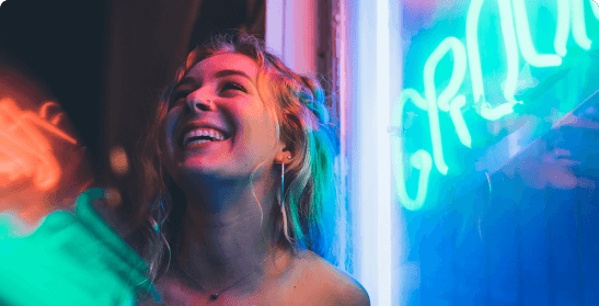 A white lady laughing  standing next to a blue neon sign