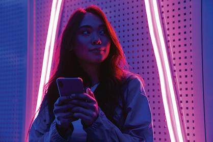 A smiling lady standing in front of neon lights holding a phone